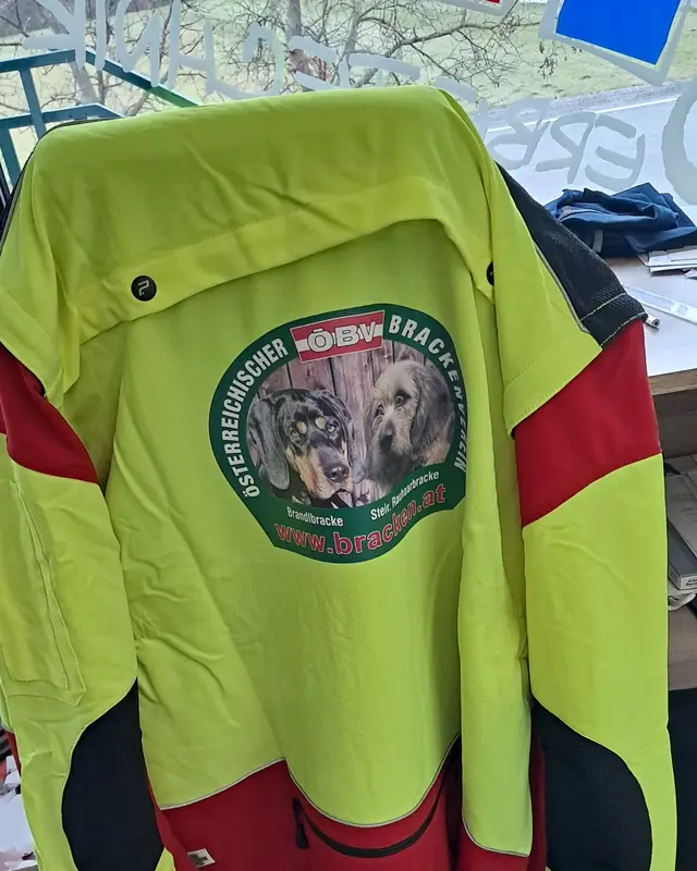 Warnfarbene Forst-Arbeitsjacke mit großem, farbigem Vereinslogo am Rücken
