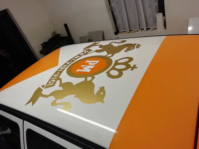 Dachfolierung mit goldenem Wappen auf einem orange-weißen Rallyeauto