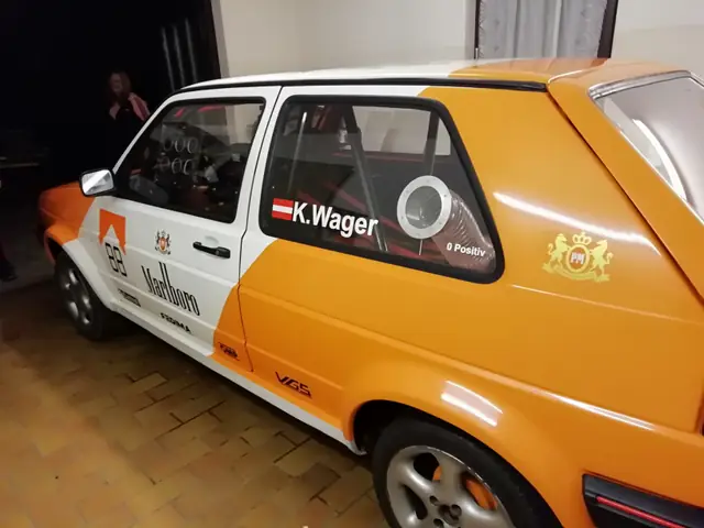 Seitenansicht eines orange-weißen Rallyeautos mit Fahrername und Startnummer